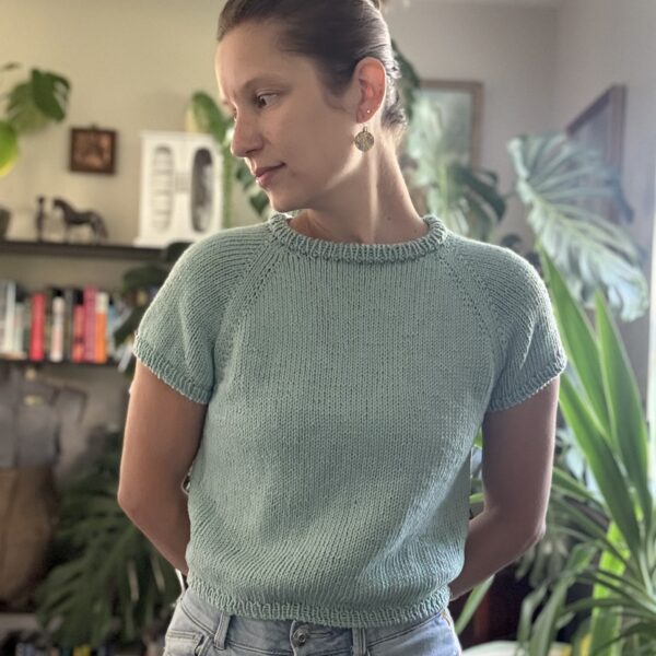 Laramie is wearing a hand knit tee shirt. The shirt is teal with short sleeves and a raglan construction. The body is slightly cropped.